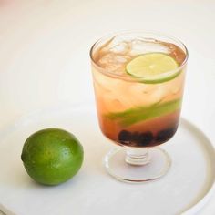 a drink with lime and ice sitting on a white plate next to a green lemon