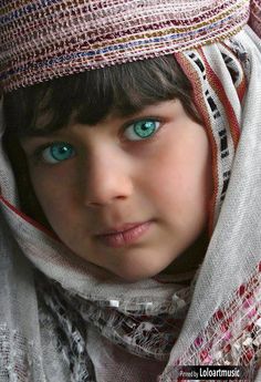 a close up of a child with blue eyes wearing a hat and scarf on her head