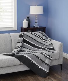 a gray couch with a black and white blanket on top of it next to a lamp