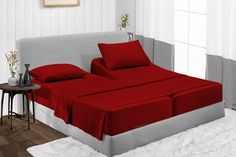 a bed with red sheets and pillows on top of it next to a white rug