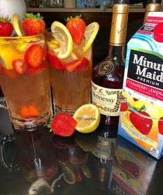 two glasses filled with liquid and strawberries on top of a table next to bottles of alcohol