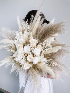 a woman holding a bouquet of white flowers and feathers in front of her face on a gray background