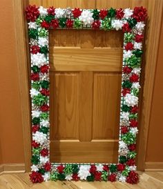 a decorated frame sitting on the floor in front of a door with red, white and green flowers