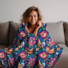 a woman sitting on top of a couch covered in a blue flowered blanket and smiling at the camera