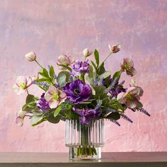 a glass vase filled with purple flowers on top of a wooden table next to a pink wall