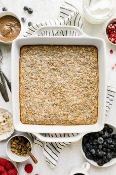 an overhead view of a baked oatmeal in a white dish surrounded by berries, nuts and yogurt