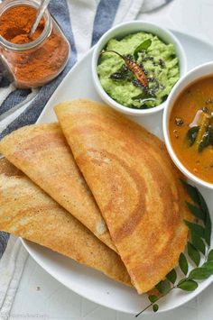 a white plate topped with three quesadillas next to bowls of guacamole