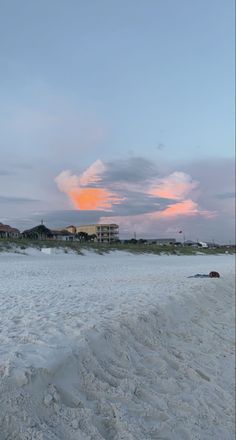 the beach is covered in white sand as the sun sets over the buildings behind it