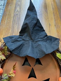 a black paper hat sitting on top of a pumpkin shaped plate with leaves around it