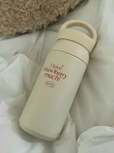 thermos bottle is laying on top of the white bed sheets and pillows next to a teddy bear