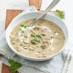 a bowl of soup with mushrooms and sour cream in it on a wooden cutting board