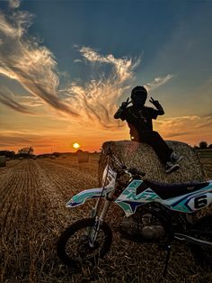 a person jumping over a bale of hay on a dirt bike in the middle of a field