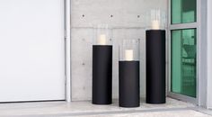 three tall black vases sitting in front of a glass door with candles on them