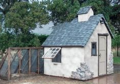 a small white building with a black roof and windows next to a fenced in area