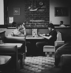 black and white photograph of two men sitting at tables in a restaurant, one reading a book