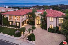 this is an aerial view of a home in the hills at dusk with palm trees and landscaping