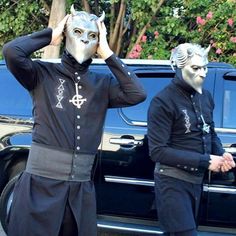 two men in costumes standing next to a black truck with their hands on their head