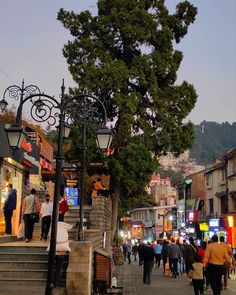 many people are walking down the street in town at dusk, with shops and stores on both sides