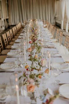 a long table is set up with white plates and silverware, candles and flowers