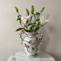 a white vase filled with flowers sitting on top of a marble table next to a wall