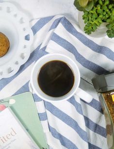 a cup of coffee sitting on top of a blue and white towel next to a cookie