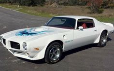 a white muscle car with blue flames painted on it's hood parked in a parking lot