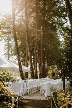 an outdoor wedding setup with white linens and tables in the woods, surrounded by tall trees