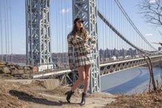 a woman standing on the side of a hill next to a tall bridge with a city in the background