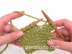 two hands crocheting the ends of a green knitted object with orange needles