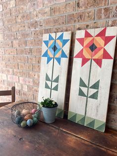 two wooden boards with flowers painted on them next to a potted plant and some eggs