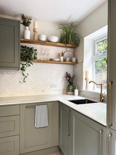 a kitchen with gray cabinets and white counter tops, plants on the shelf above the sink