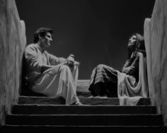 a man and woman sitting on the steps in front of each other looking at something