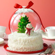 a snow globe with a small christmas tree in it on top of a table next to cups and saucers