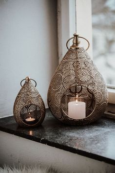 two candles sitting on top of a window sill next to a vase with a candle in it