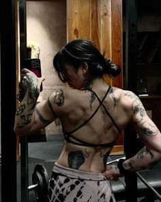 a woman with tattoos on her back holding a barbell and looking at her cell phone