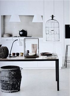 black and white photograph of kitchen with table, stools and birdcage in background