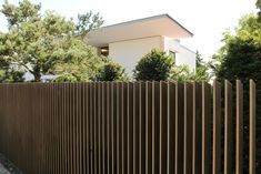 a tall brown fence next to a white house and some trees in front of it