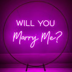 a purple neon sign that says will you marry me? in front of a dark background