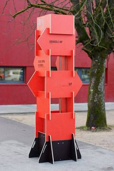 a tall red sign sitting on the side of a road next to a tree in front of a building