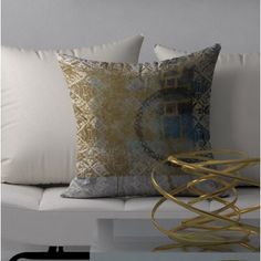 two decorative pillows on a white couch in front of a wall with gold and silver accents