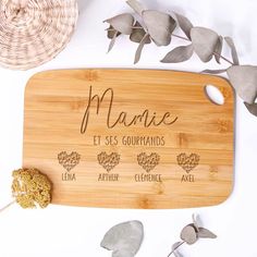 personalized cutting board with names and hearts on it next to dried leaves, wicker basket and potted plant