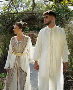 a man and woman dressed in white walking down a path