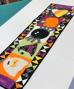 a colorful table runner with black cats and pumpkins in the center on a white surface