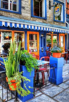 an outdoor cafe with colorful tables and chairs in front of the storefront, filled with potted plants