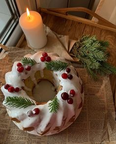 a cake with icing, pine and cherries on it next to a lit candle