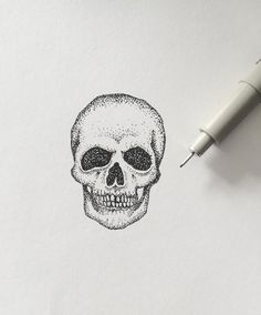 a drawing of a skull on paper next to a pen and inking tip,