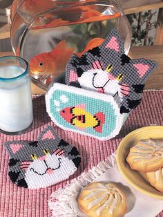 cross - stitch cats and fish coasters on a table next to a glass of milk