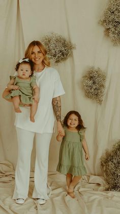 a woman holding a baby and standing next to two other women in front of a backdrop