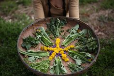 a woman holding a basket full of flowers on the ground with grass and weeds around it