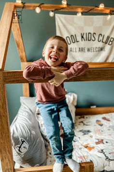 a young boy standing on top of a wooden bed frame with lights strung from the ceiling